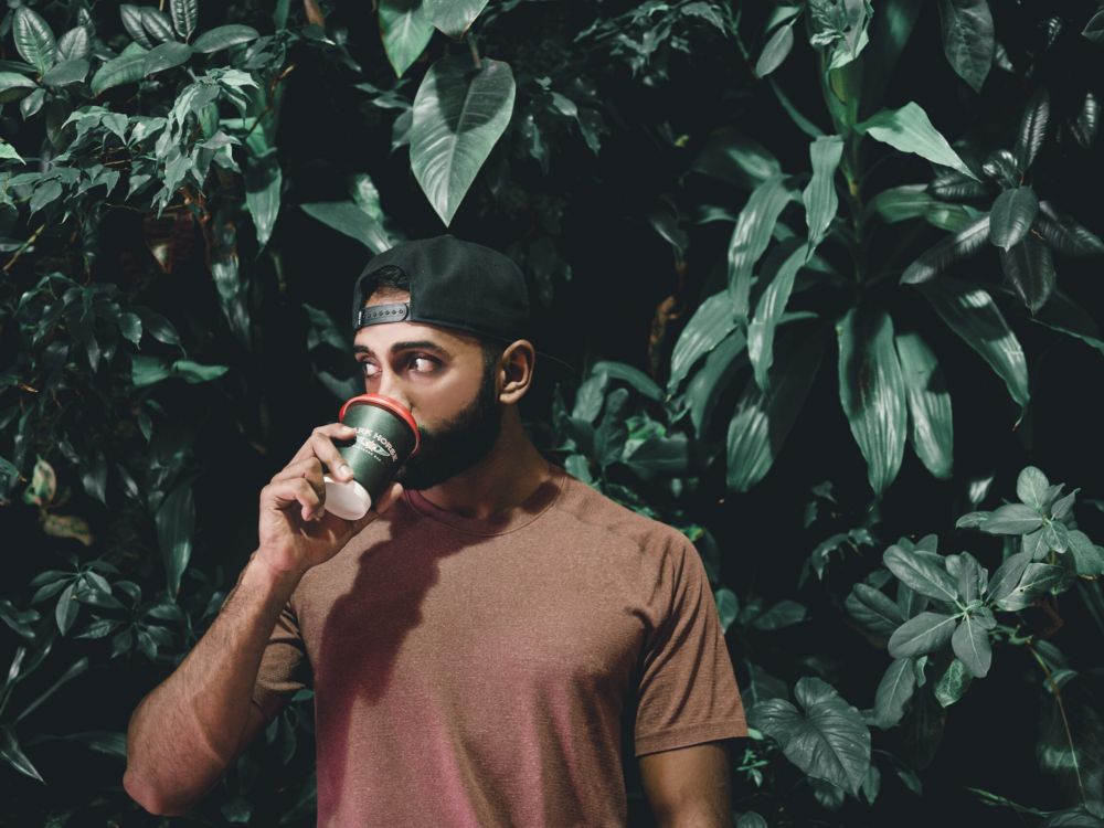 Man drinking a cup of coffee in front of a plant wall