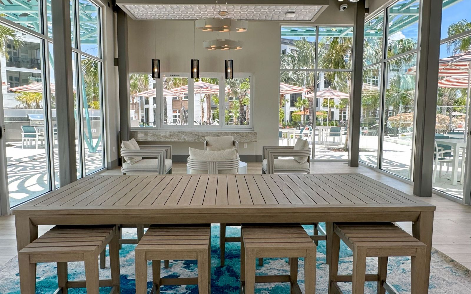 Modern wood table with designer lighting and floor-to-ceiling windows facing the pool