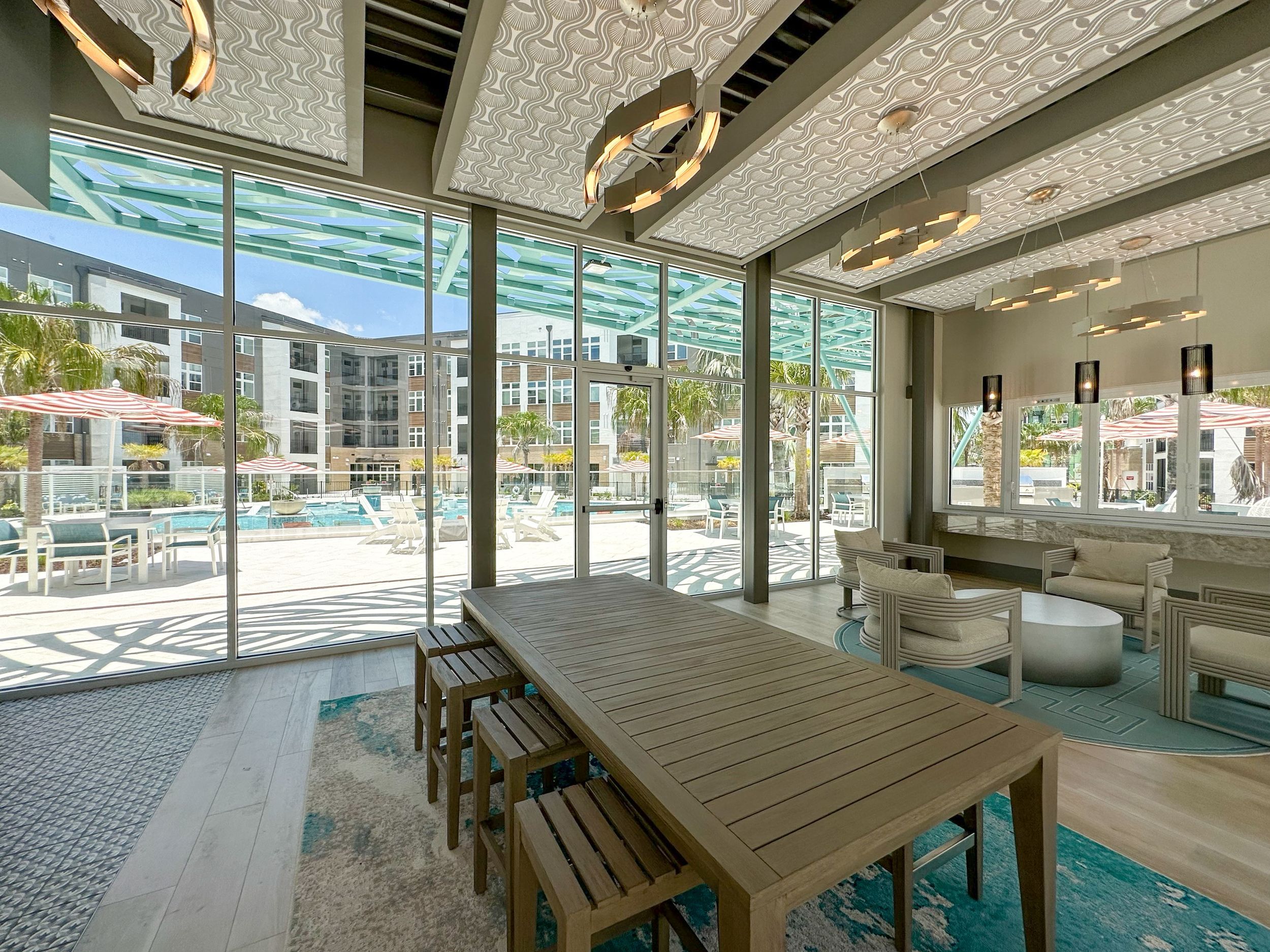Modern wood table with designer lighting and floor-to-ceiling windows facing the pool
