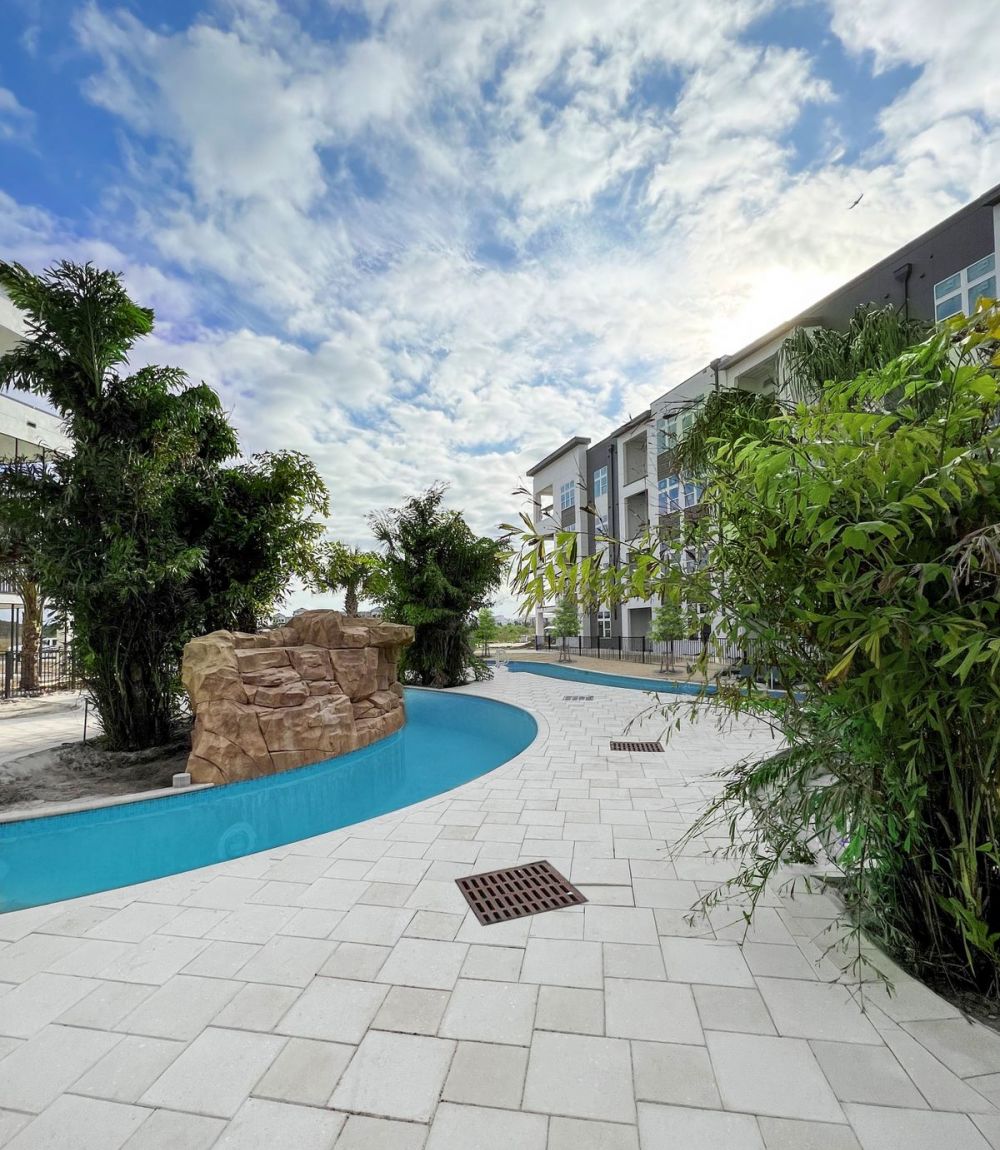 Lazy river surrounded by lush green trees with The Lucent at Sunrise apartment building next to it