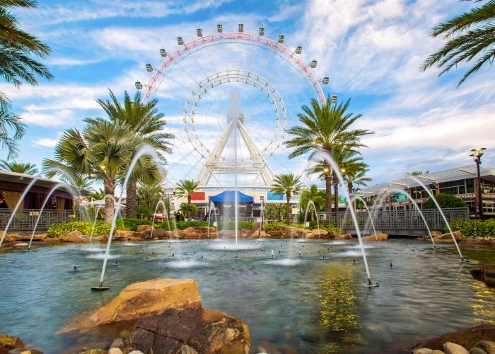Large ferris wheel behind a pool, fountain, and palm trees in Orlando, Fl