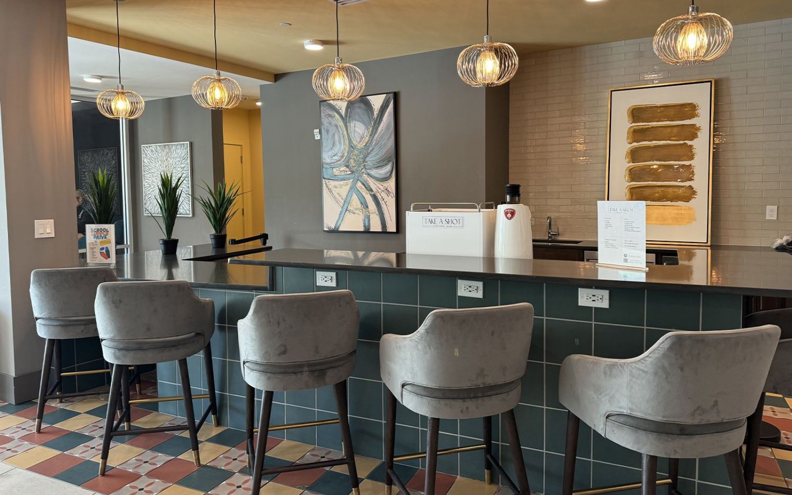 A modern hotel lobby bar with grey upholstered chairs, a dark counter, and contemporary hanging light fixtures.