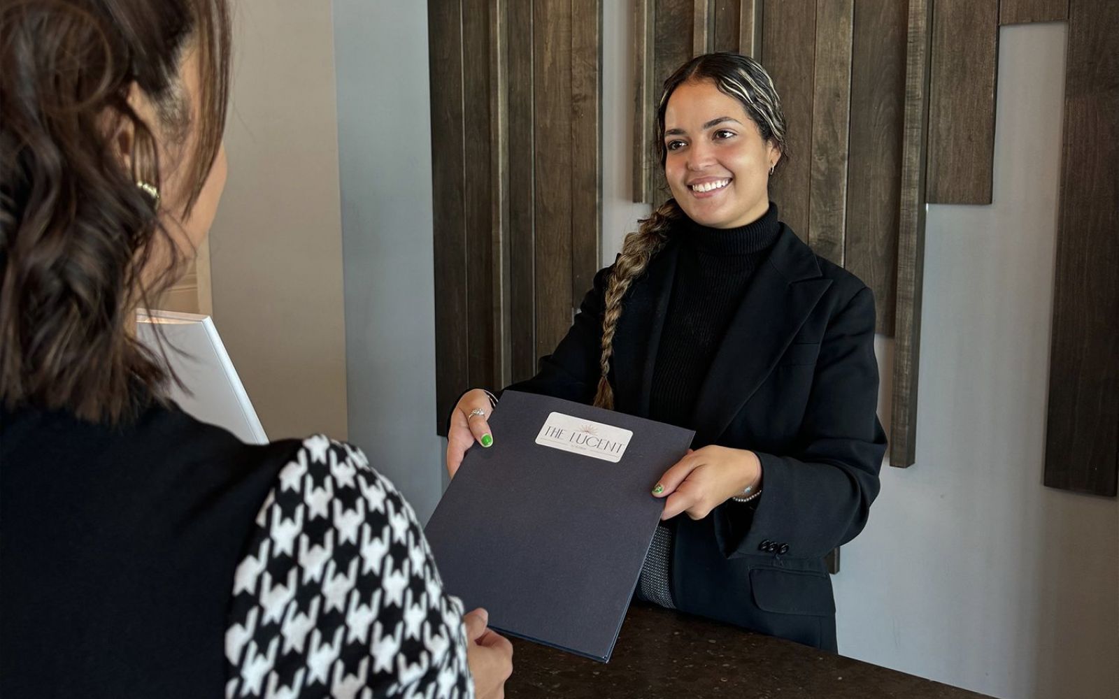 Two women in a professional setting, smiling and holding a document folder at a desk.
