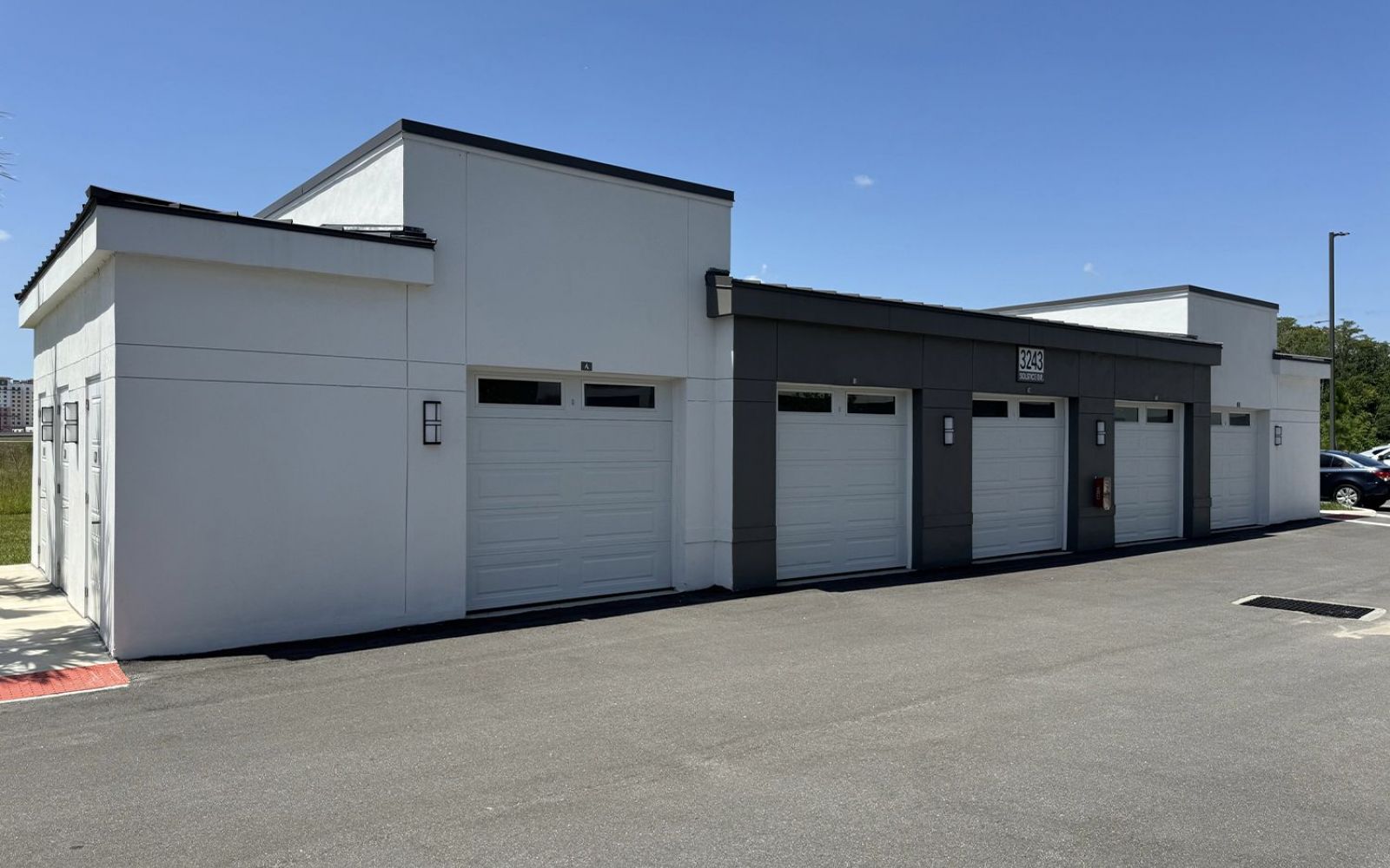 A row of closed garage doors in a building, with a clear blue sky overhead and no visible vehicles.